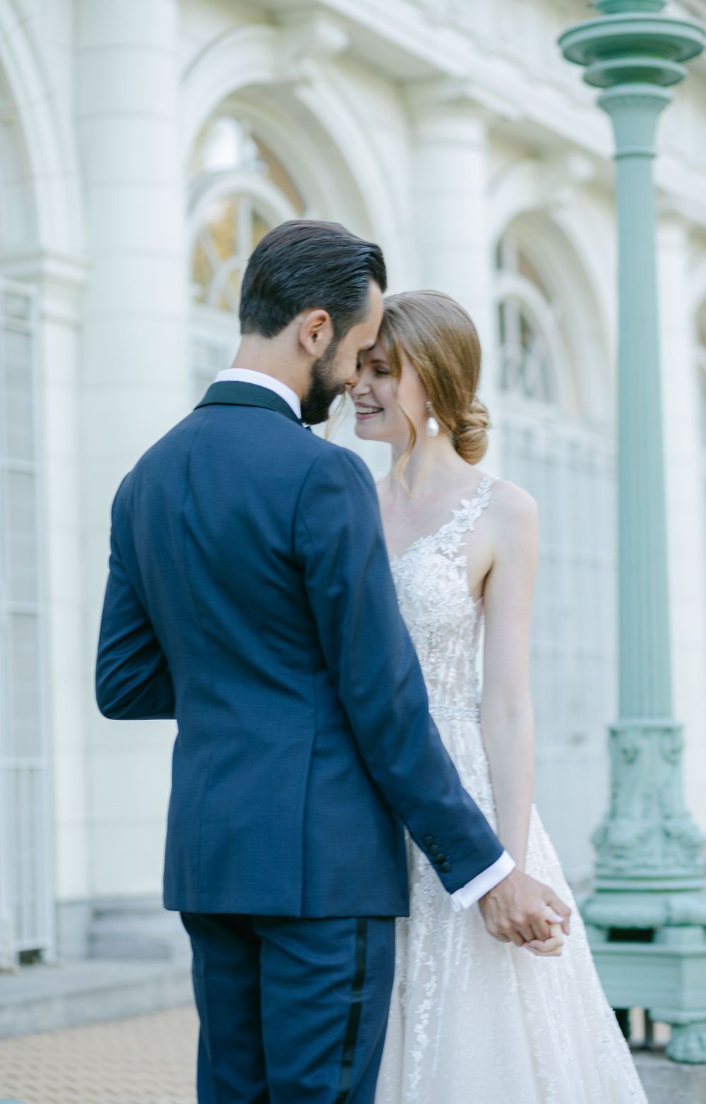 An elegant couple shares an intimate moment outside a classical architectural venue.