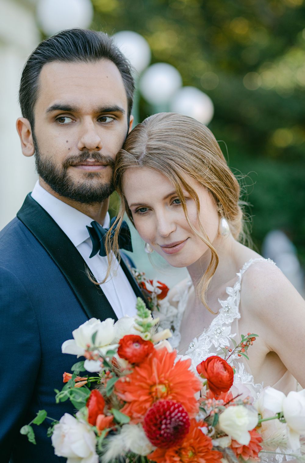 A wedding portrait with vibrant orange and red floral bouquet against white columns.