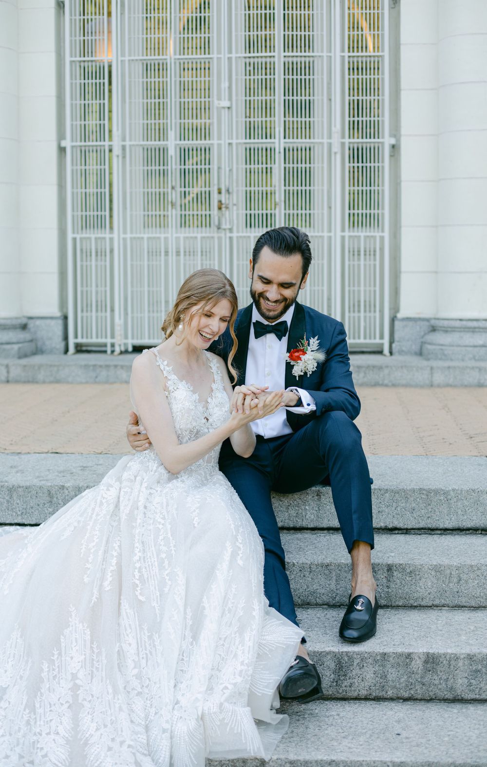Newlyweds sharing intimate moment on stone steps while looking at wedding rings.