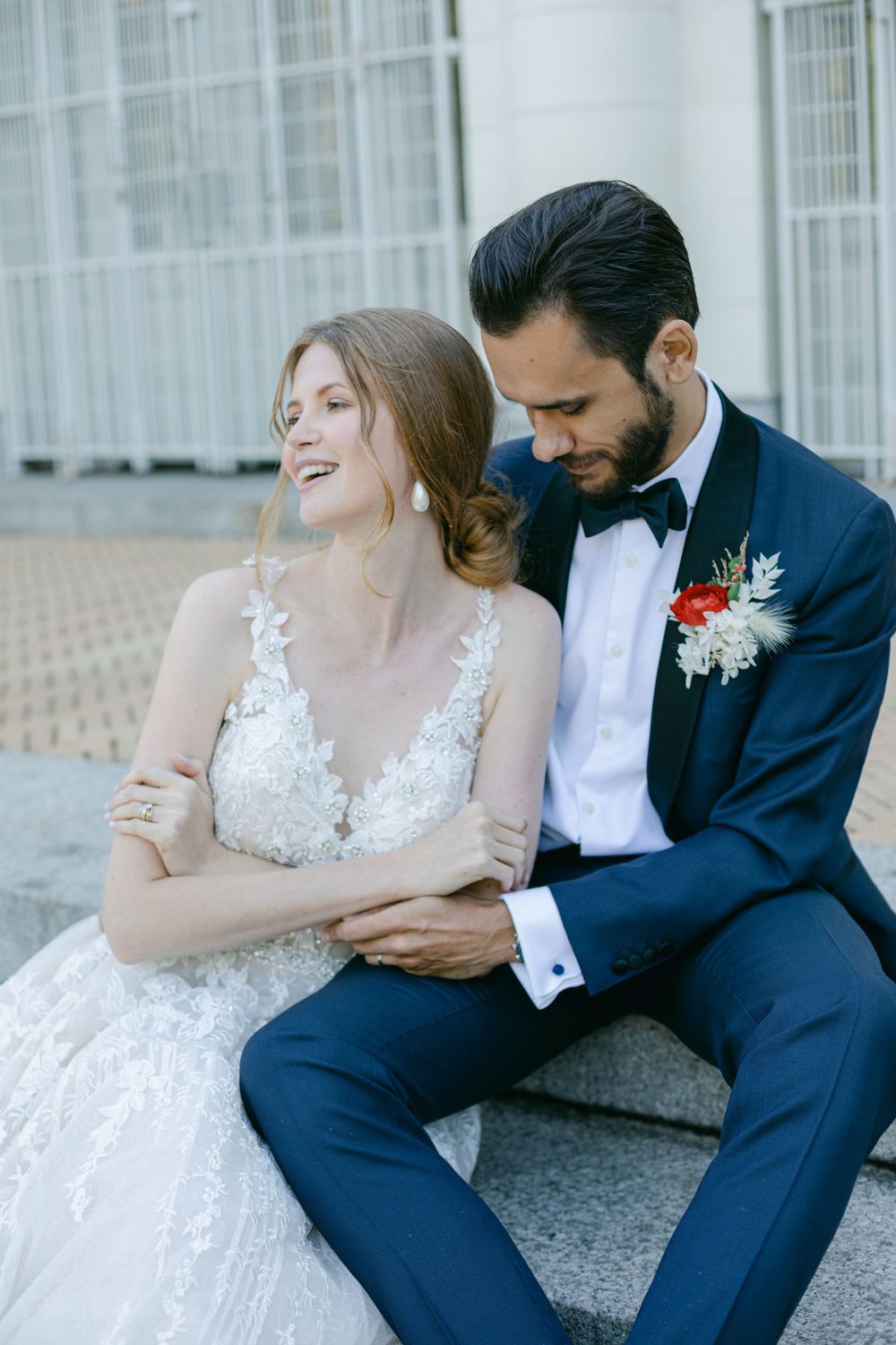Romantic portrait of newlyweds sitting together, groom in navy suit and bride in lace wedding dress.