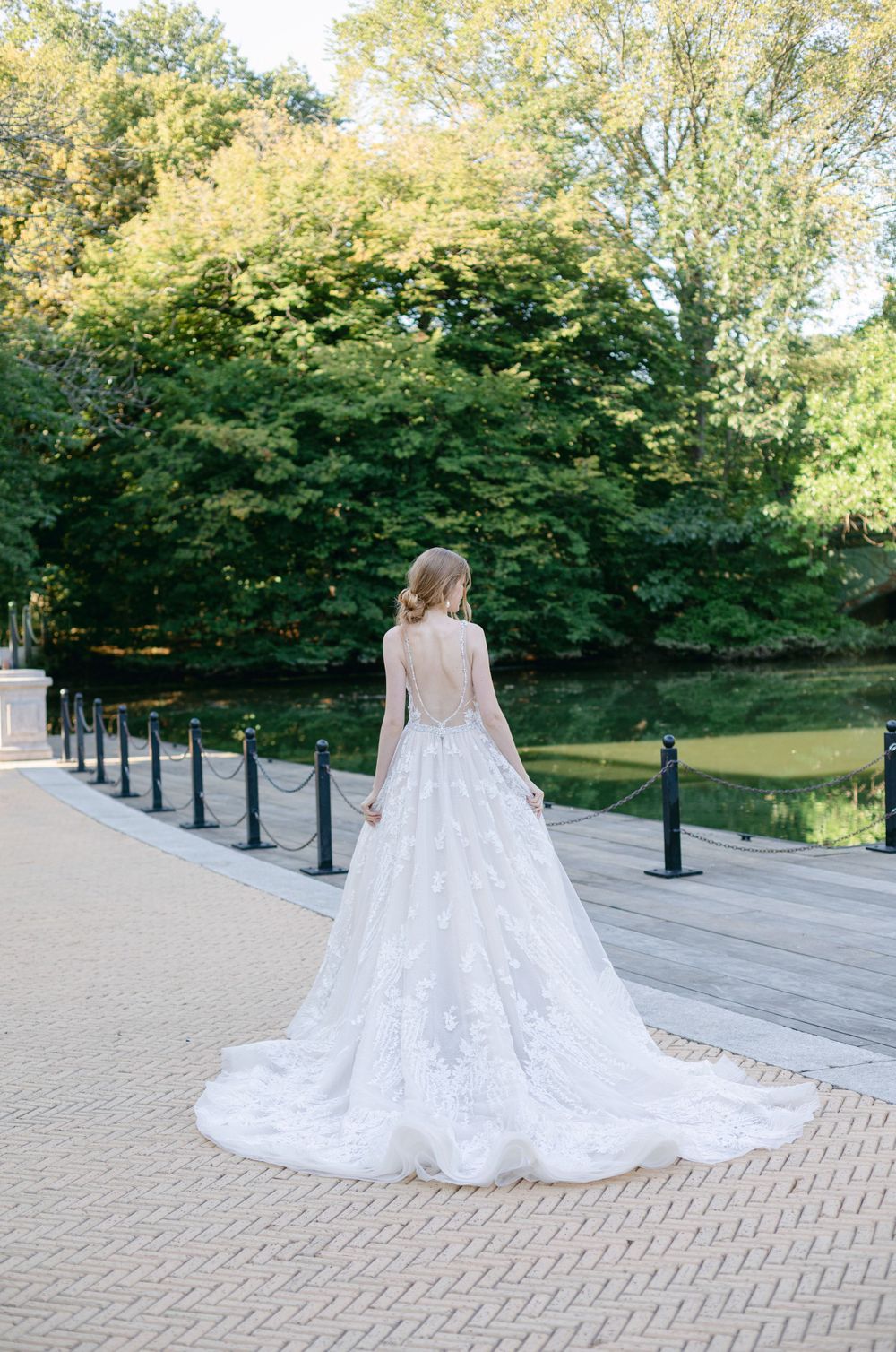 Back view of wedding dress with dramatic train on stone pathway near garden setting.