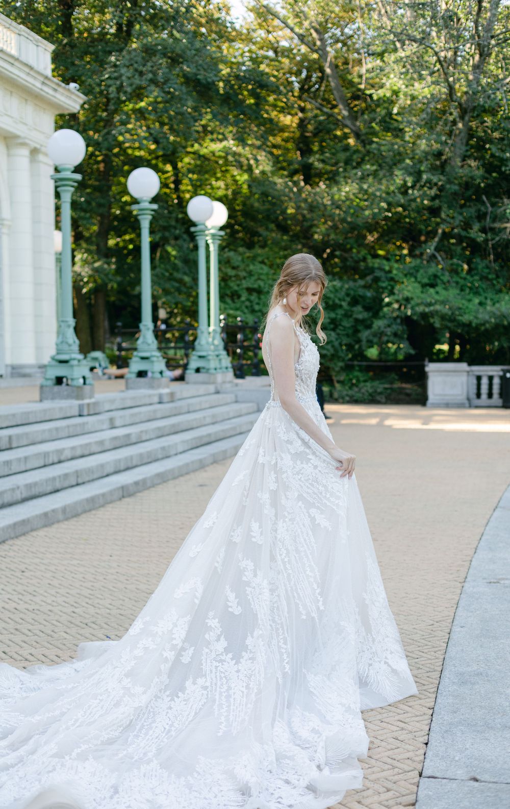 Full-length view of lace wedding gown with cathedral train beside classic lamppost.