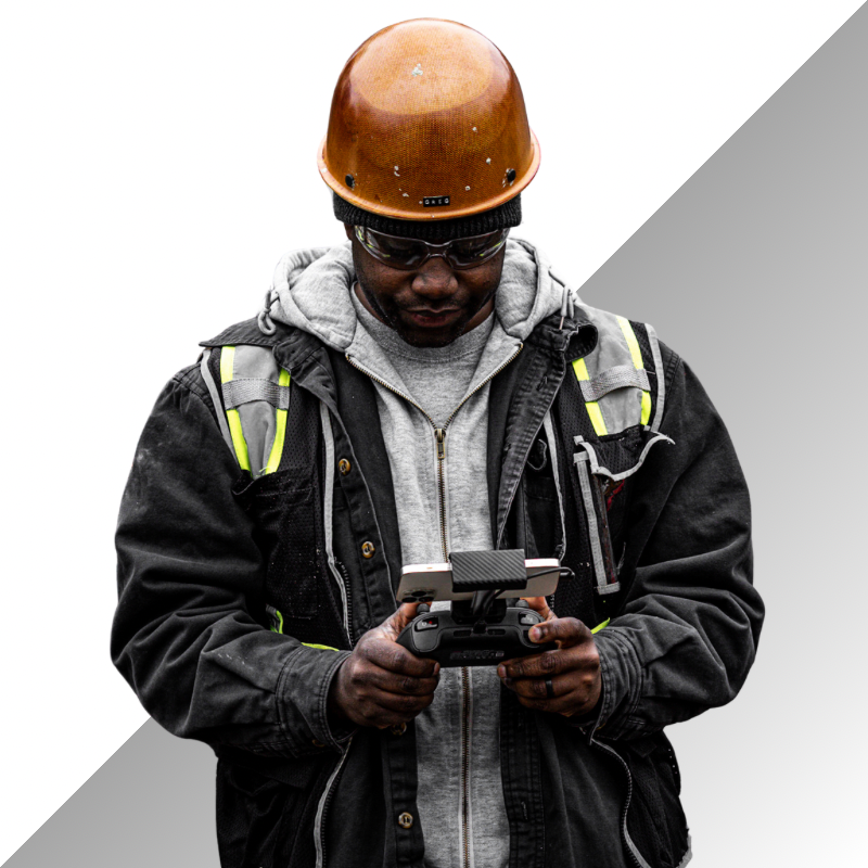 Construction worker in safety gear operating remote control equipment against gray background.