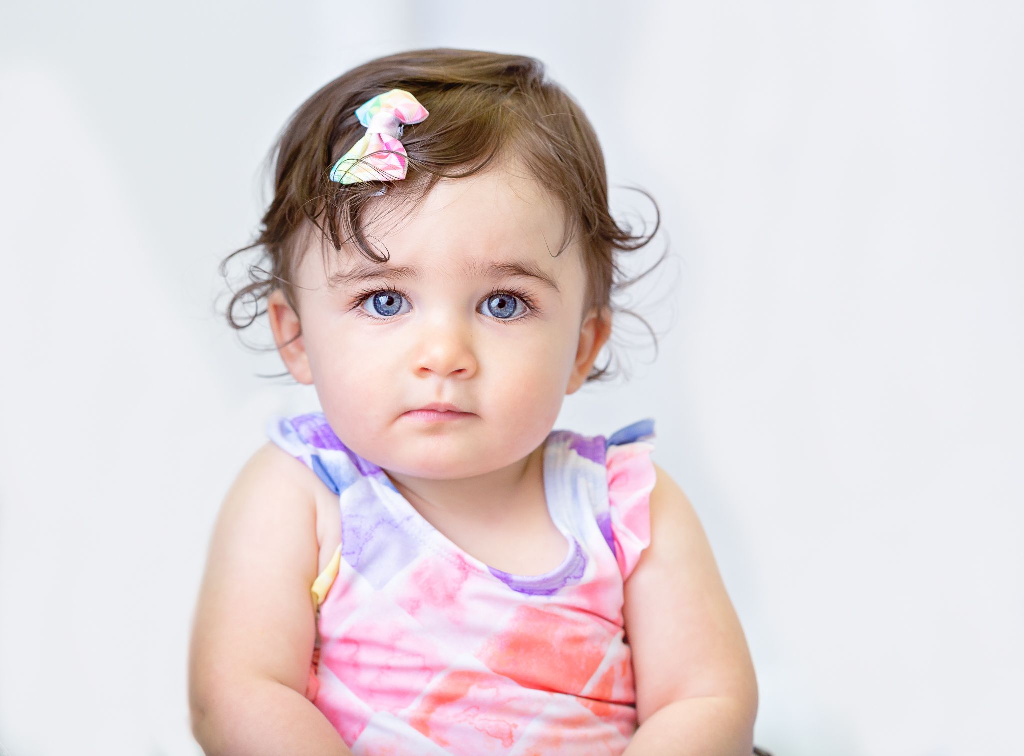 Baby in pink and white striped outfit with hair bow against white background.