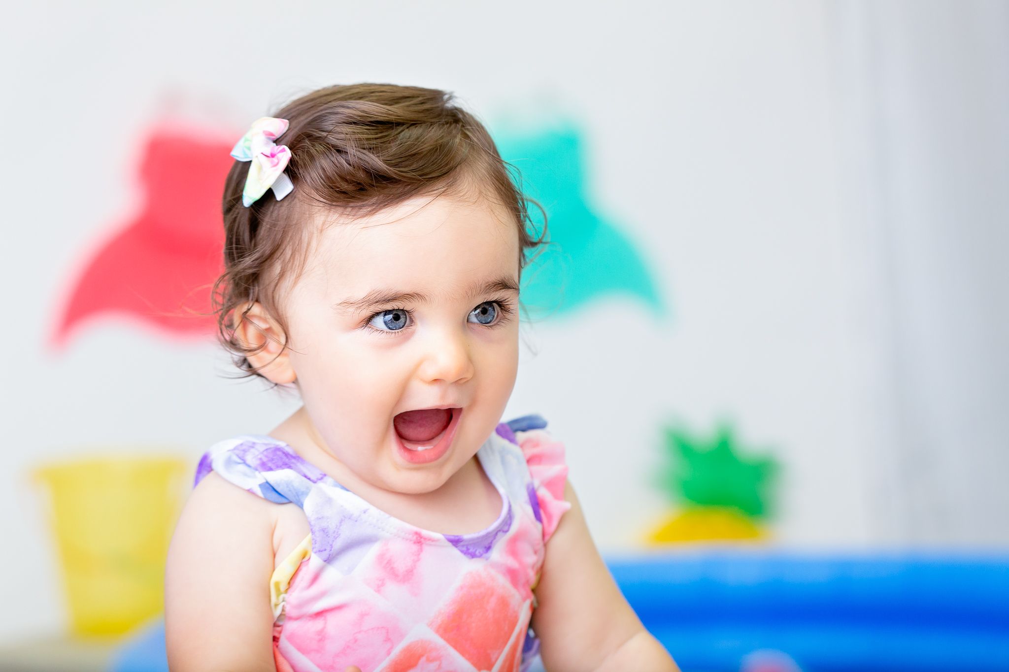 Baby in pink summer outfit smiling and playing against colorful background.
milestone photography
