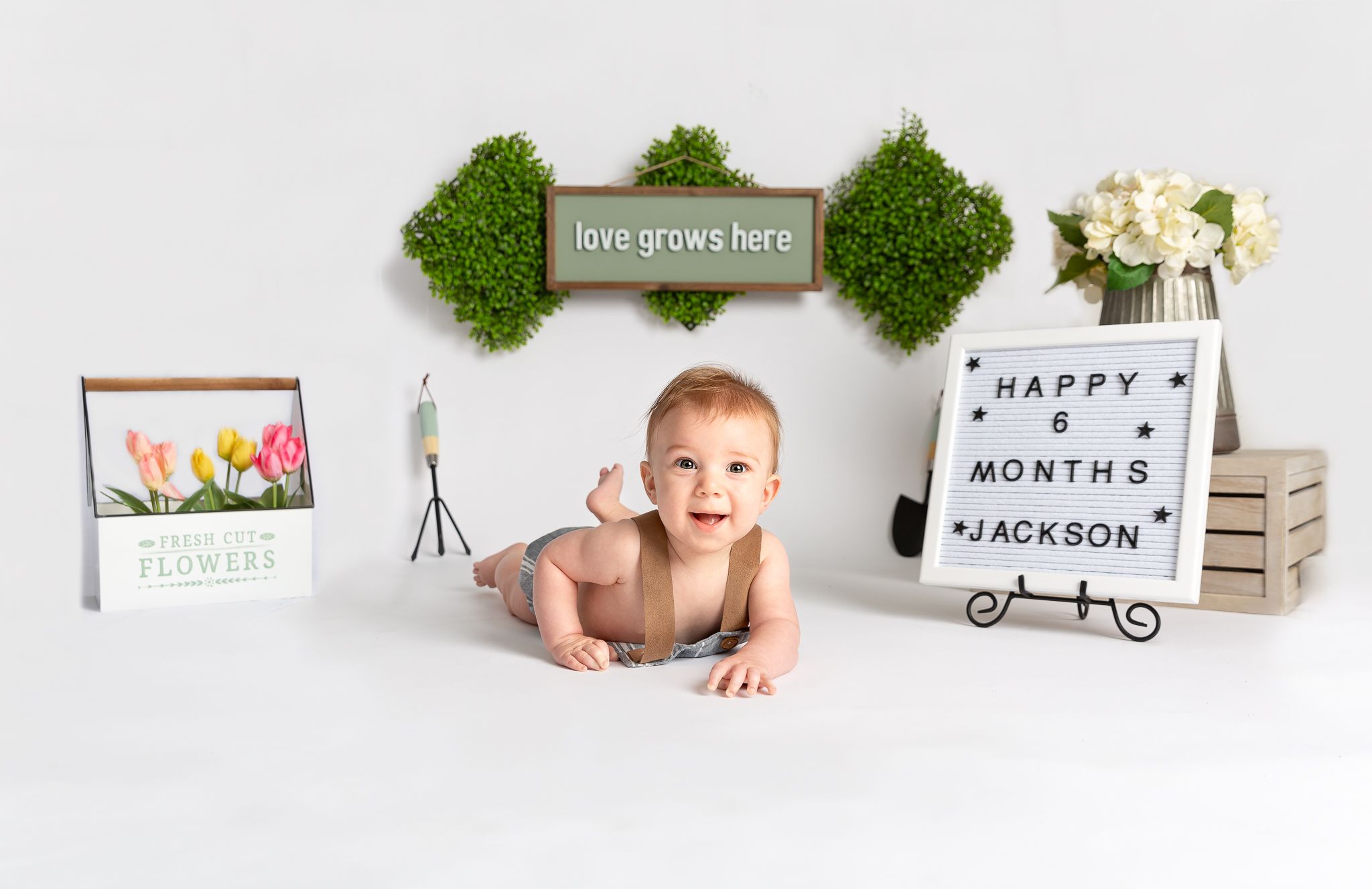 Minimalist baby milestone photography setup with wooden props and greenery.