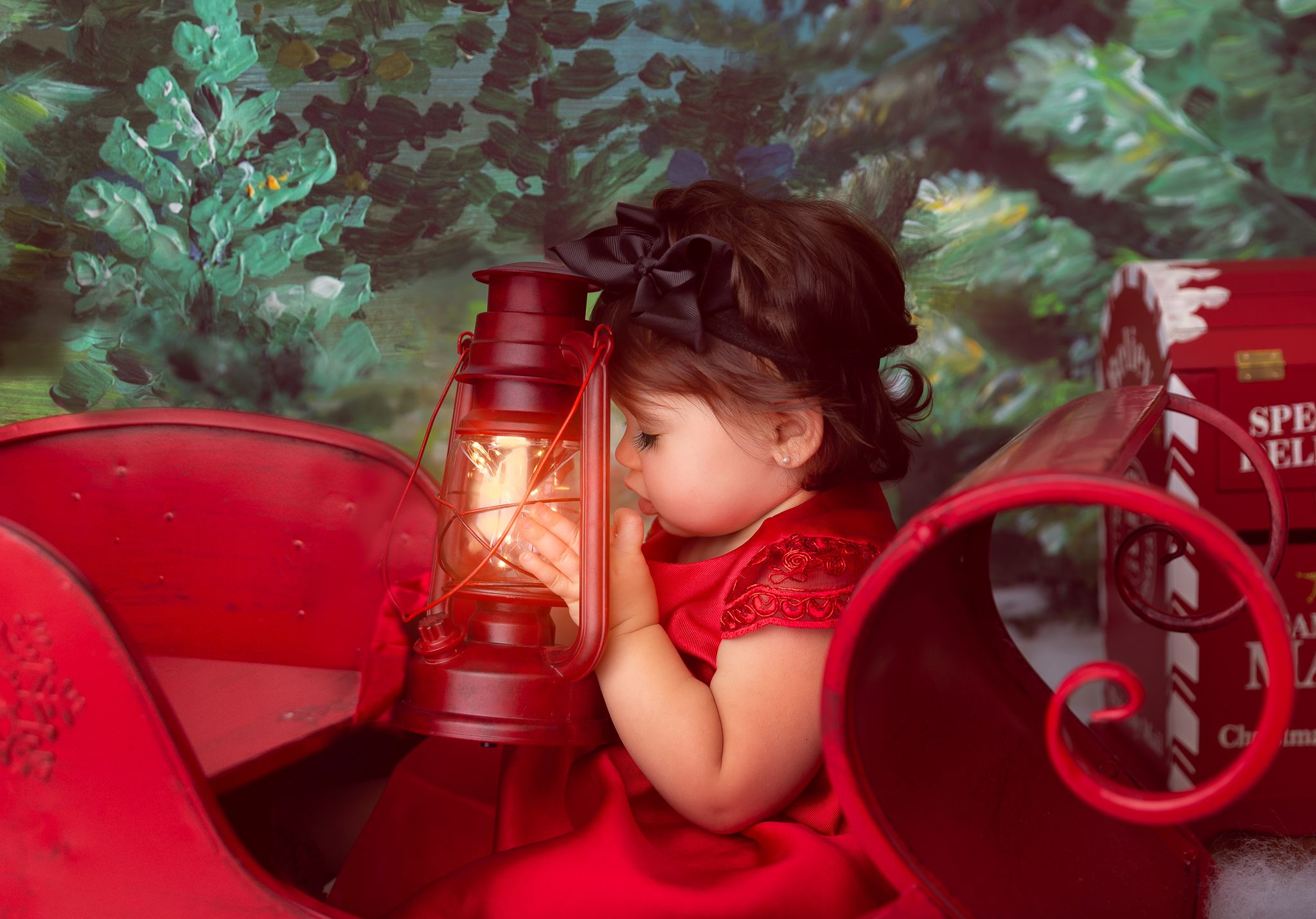 Baby in red outfit resting near vintage red lantern with dramatic lighting.