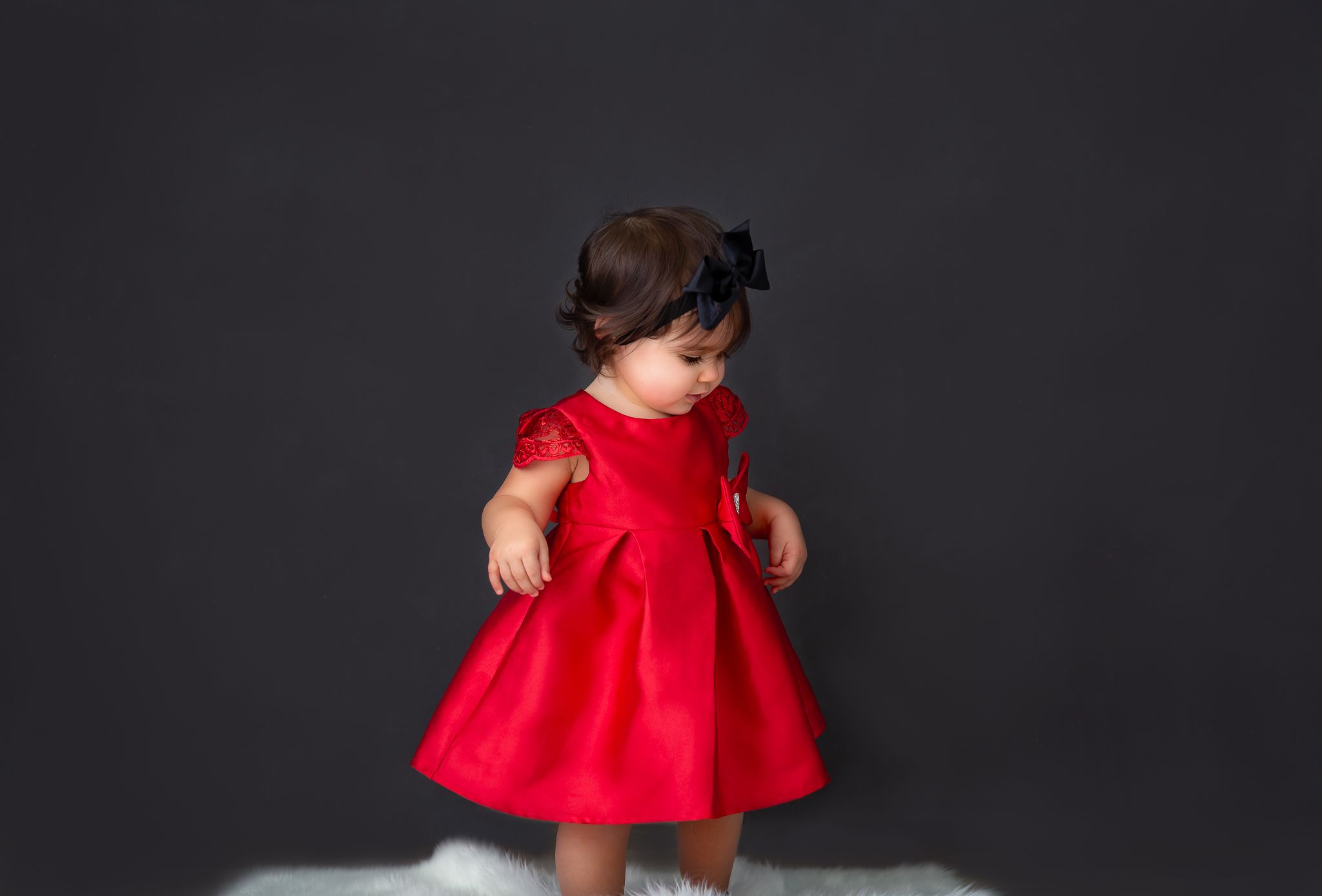 Baby in red dress twirling against dark background in studio setting.