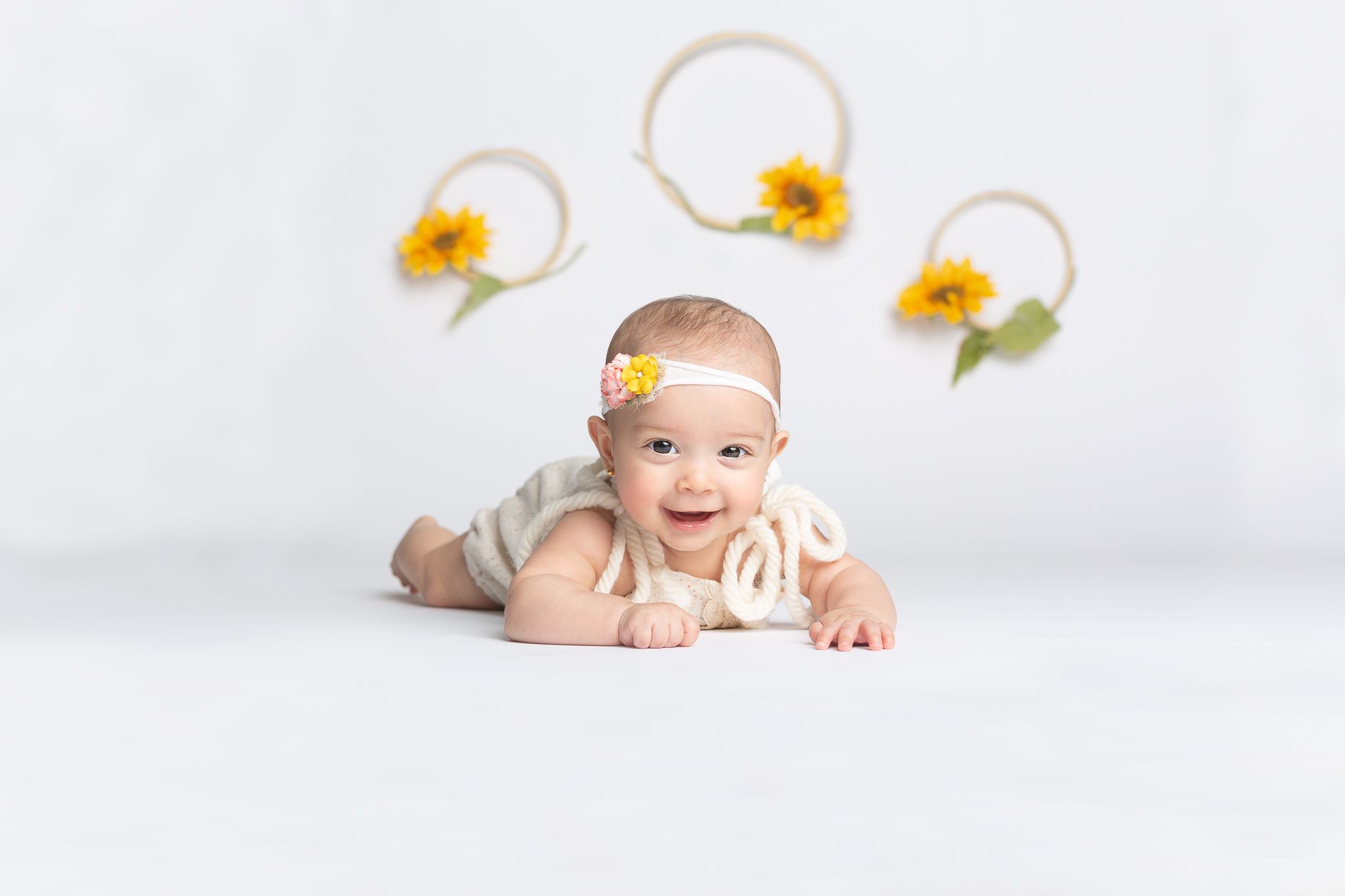 Baby in white outfit with yellow flower headband on light background.