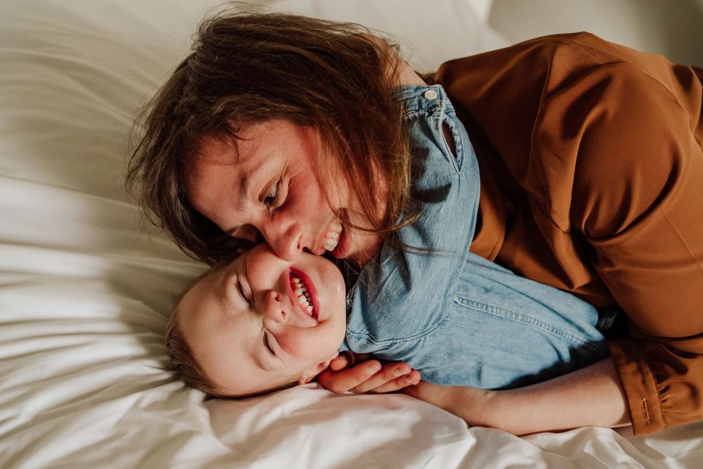 mama en zoon liggend en spelend knuffelen in bed