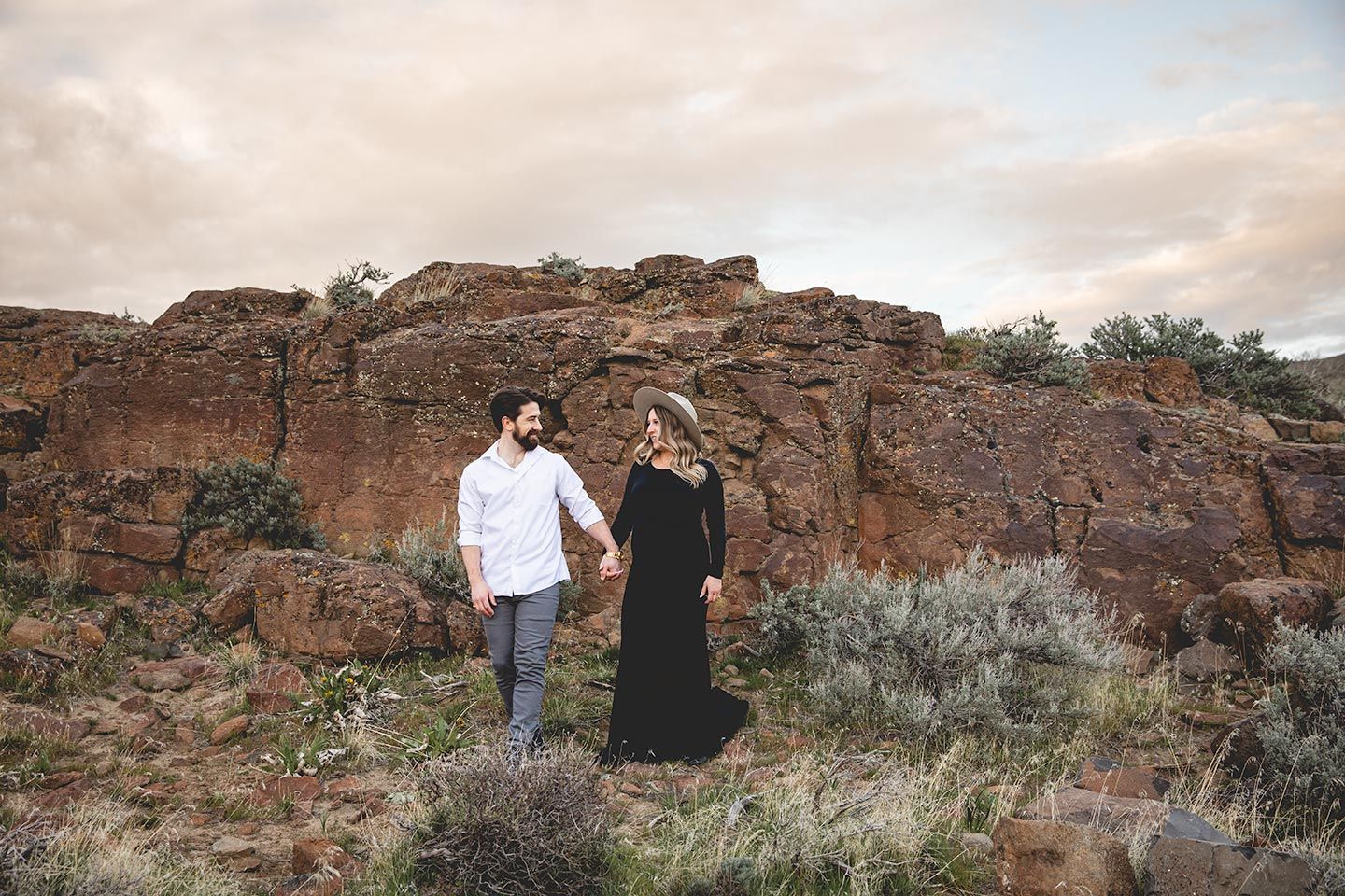 pregnant mom holding husband's hand in front of rocks at the columbia river