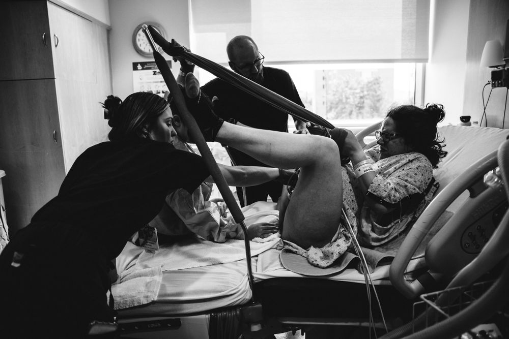 Black and white photo of woman in active labor pulling rope in hospital delivery room.