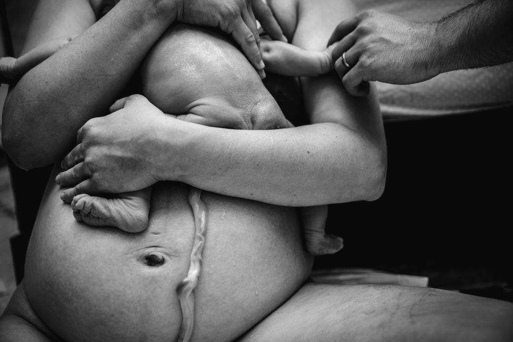 Black and white photo of newborn baby being held against mother's postpartum belly.