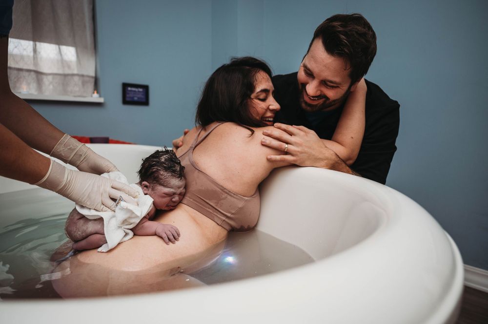 Water birth photo of couple welcoming newborn baby in birthing tub.