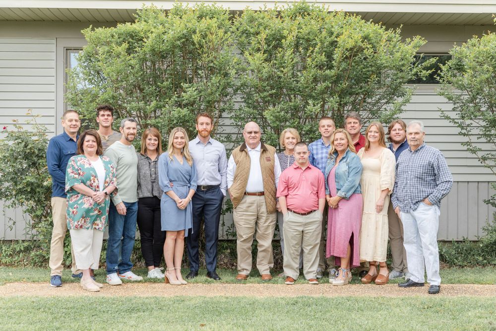 Large group photo of people sitting outdoors in front of a gray house.