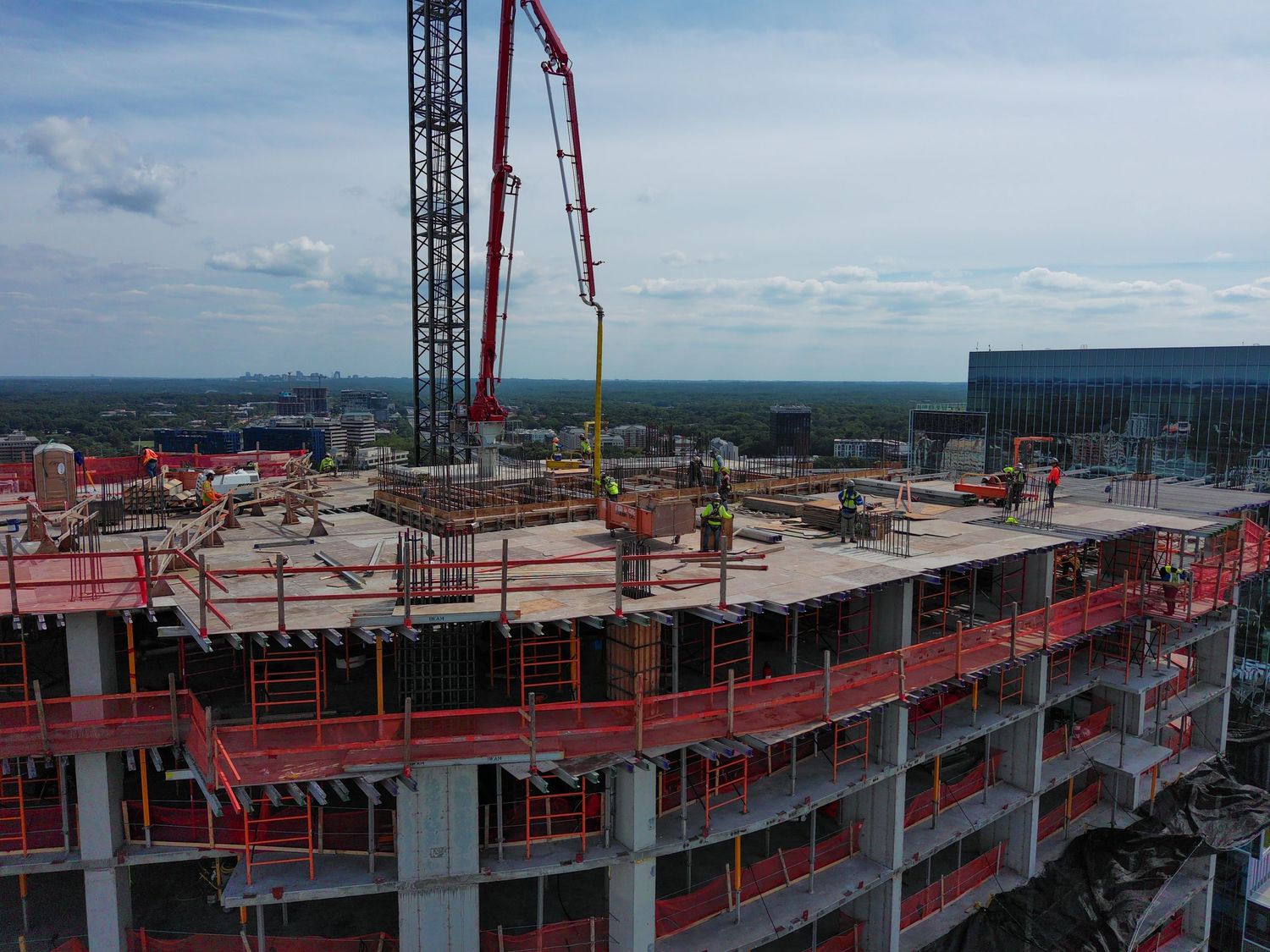 High-rise building under construction with red safety barriers and crane visible against cloudy sky.