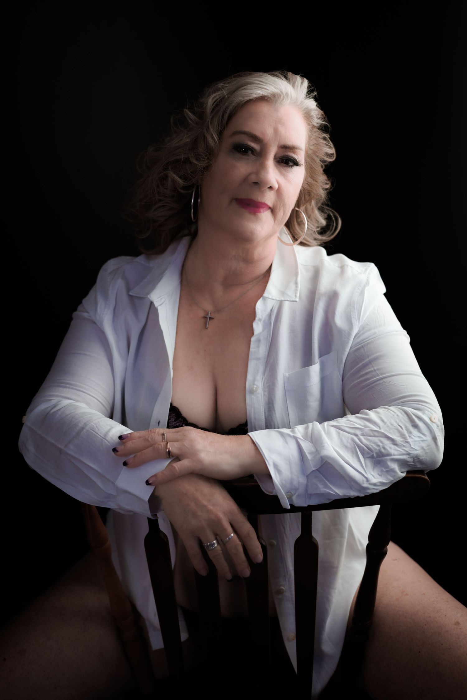 Elegant portrait of woman in white button-down shirt on dark chair.