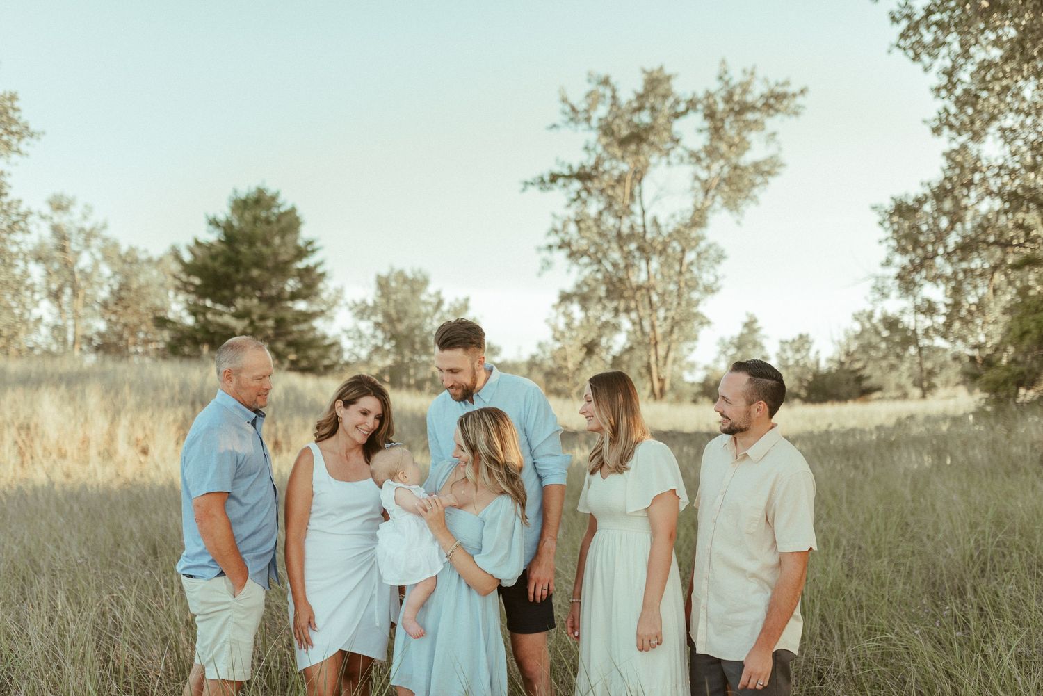 Family portrait in a sunlit field wearing coordinated blue and white outfits.