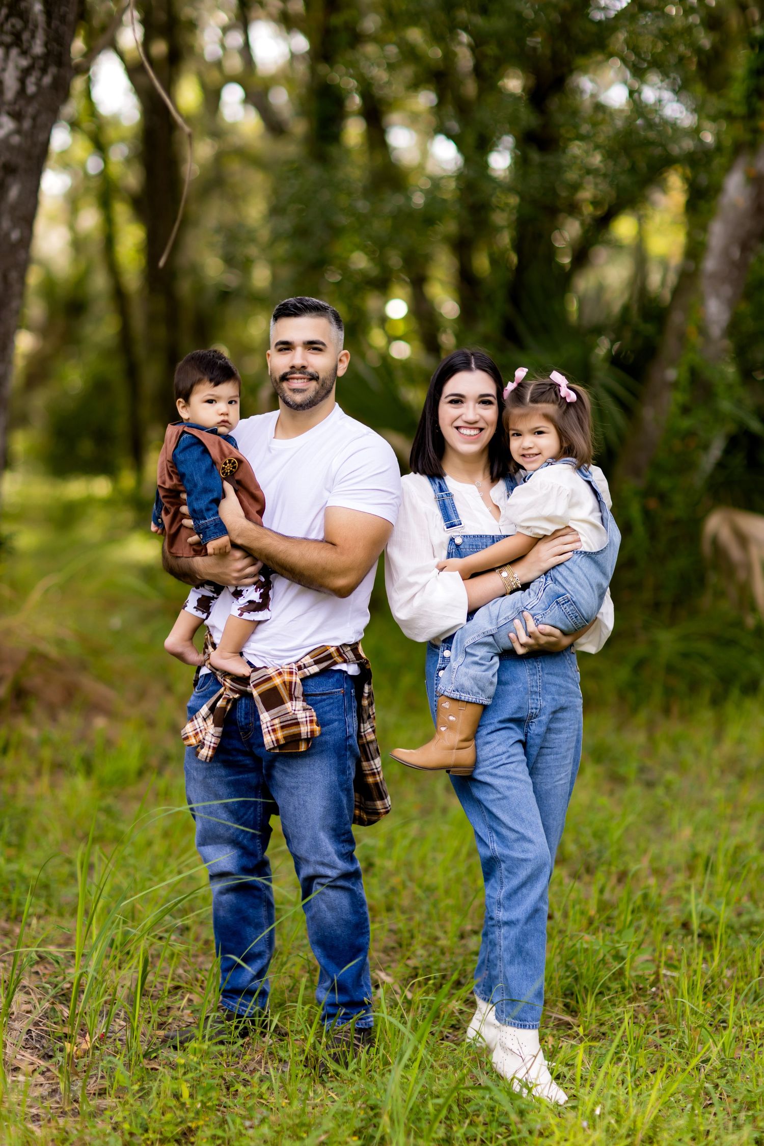 Family stands together on grassy woodland path in casual denim outfits.
