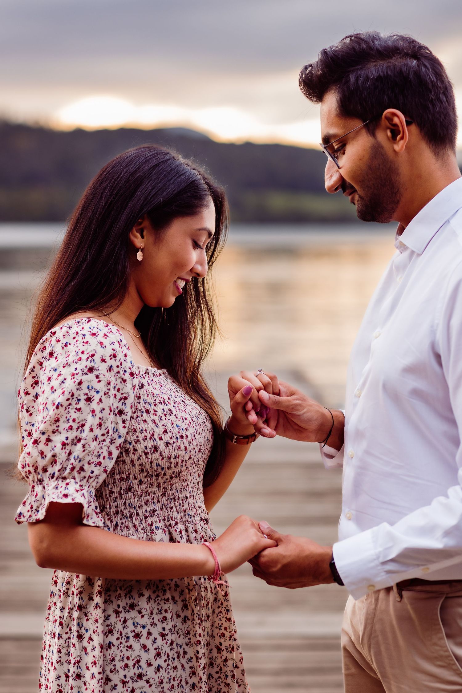 A romantic proposal scene at sunset on a wooden dock by the water.