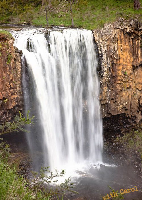 Wide waterfall streams down orange rock face creating dramatic natural scene.
