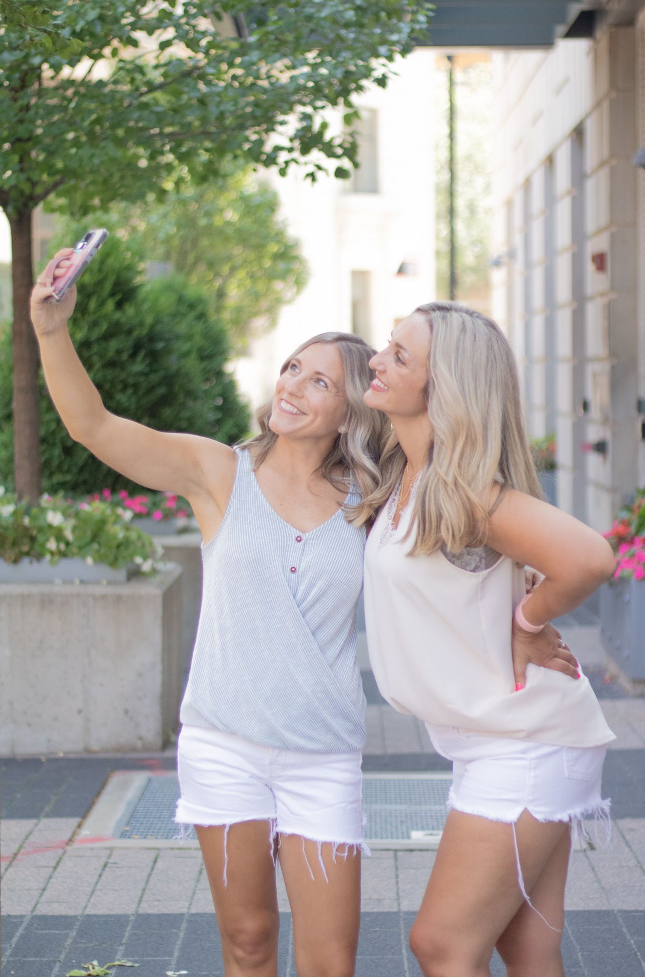 Friends taking selfies together on a sunny day in an urban setting.