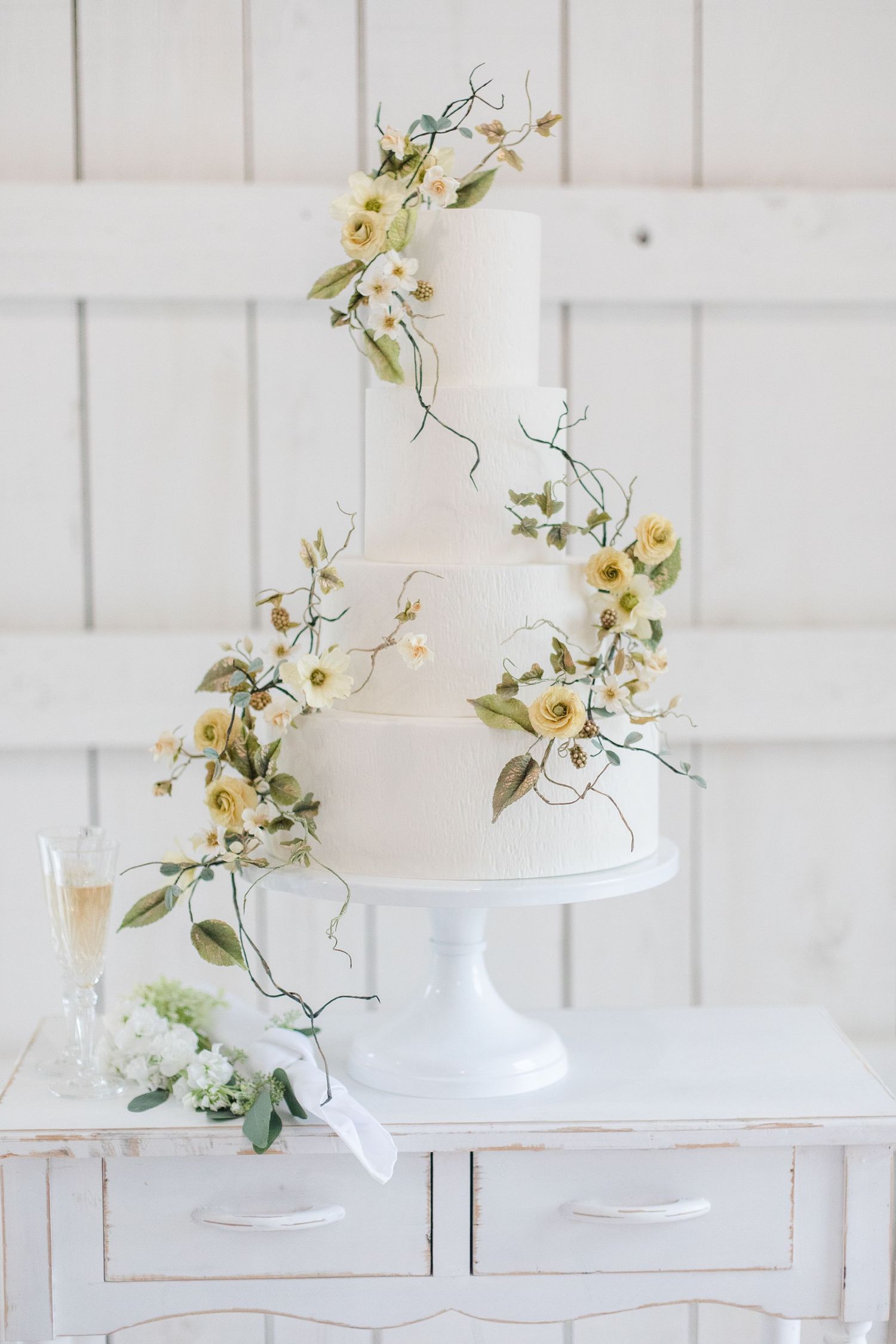 Elegant white floral arrangement with delicate vines displayed against white wooden panels.