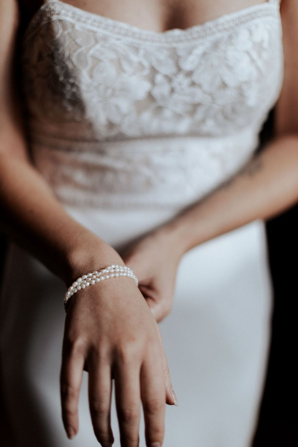 Detail shot of delicate lace bodice and pearl bracelet on a wedding dress.