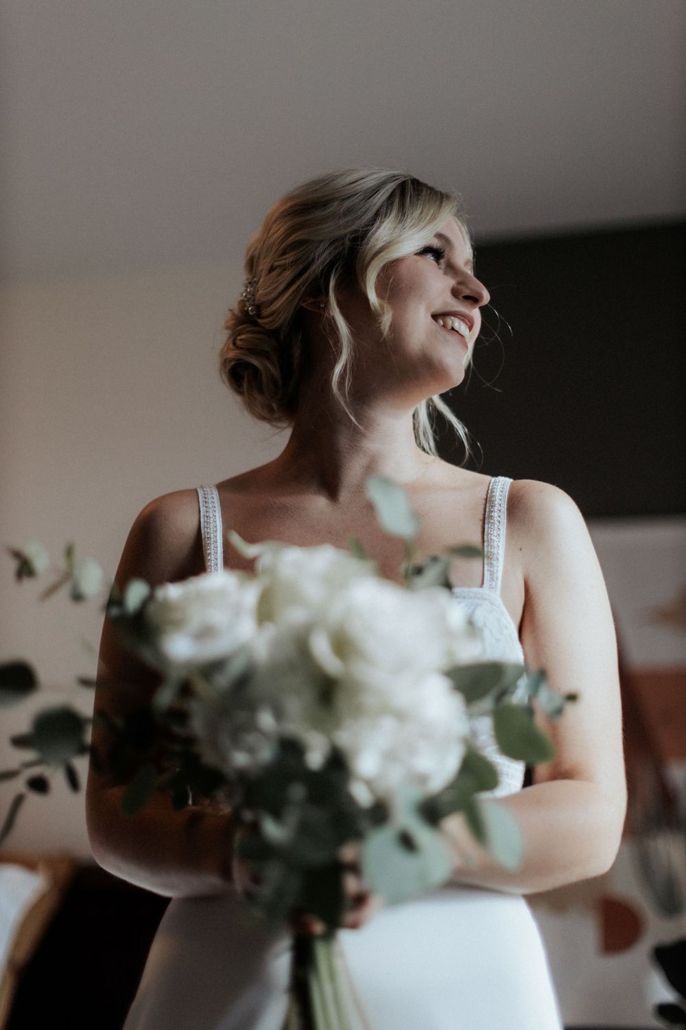 A joyful bride holding a white rose bouquet in her wedding dress.