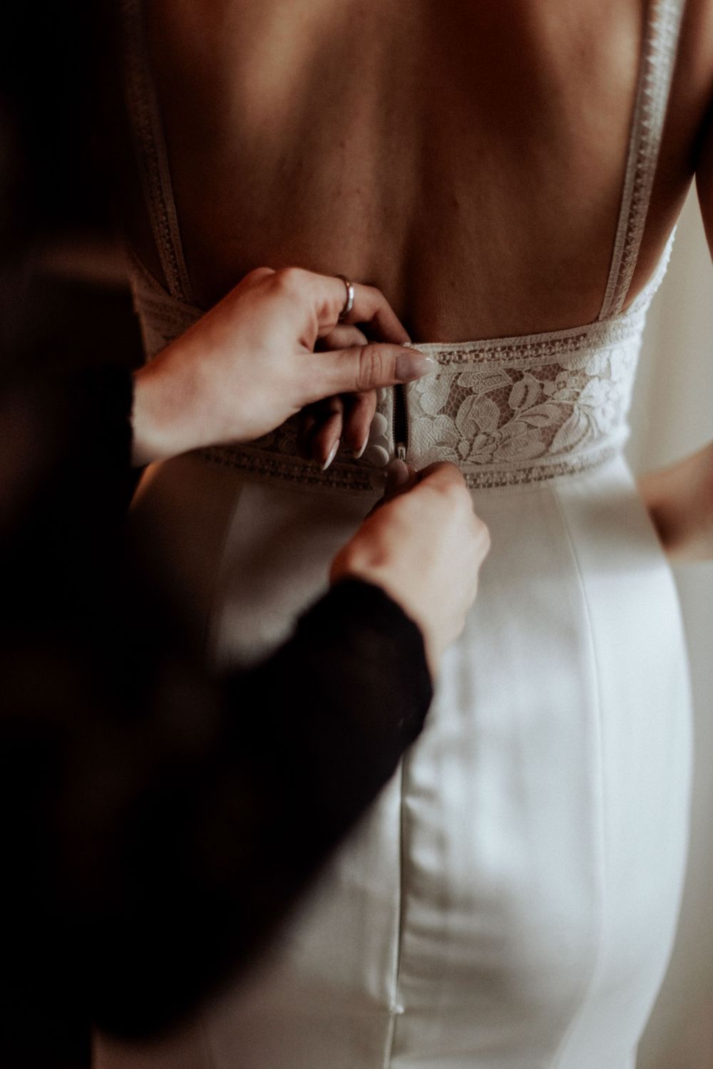 Close-up of hands fastening the detailed back of a white wedding gown.