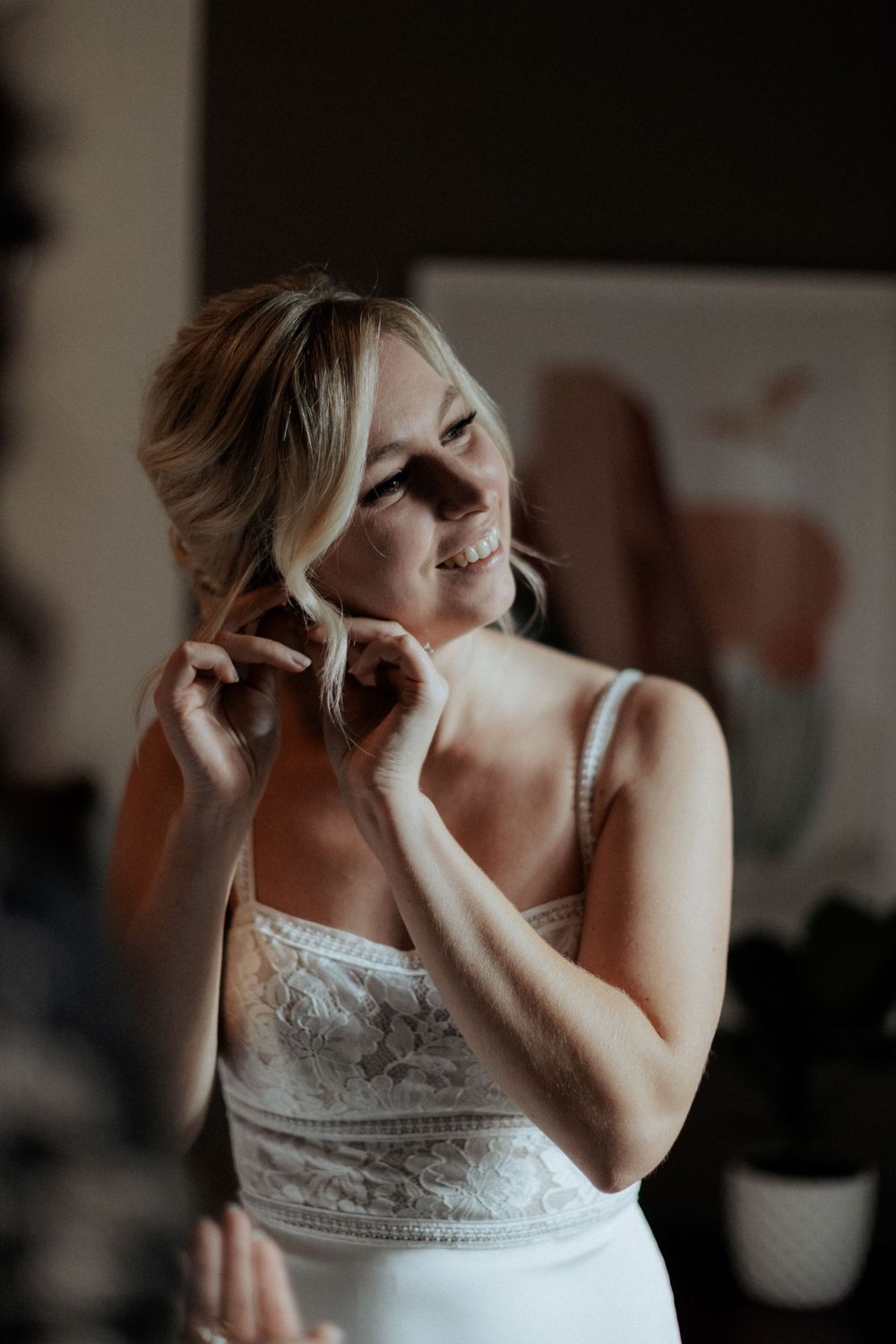 A bride adjusts her hair while wearing a fitted white wedding gown with lace bodice.