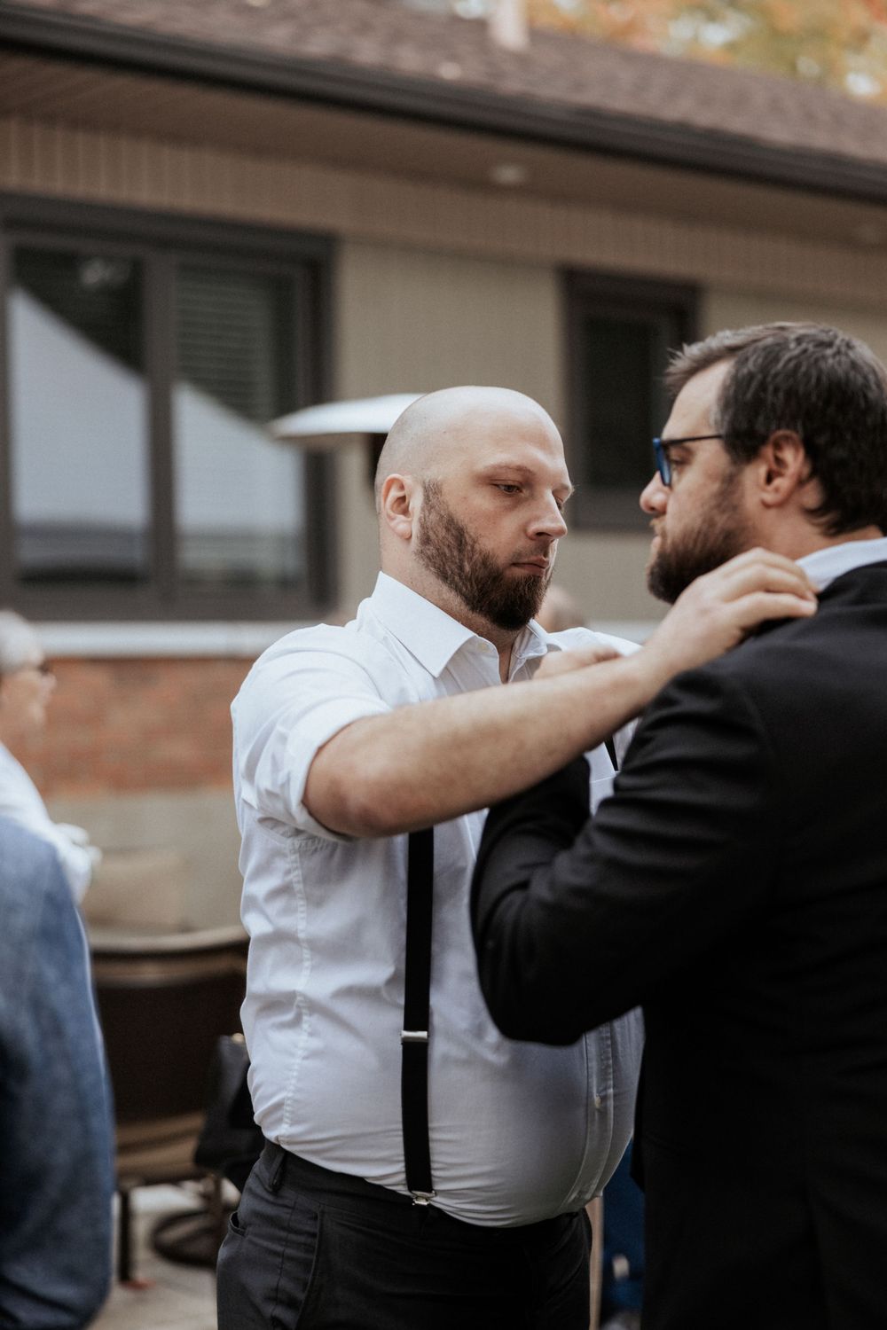 Two men in formal attire adjusting clothing during pre-wedding preparations.