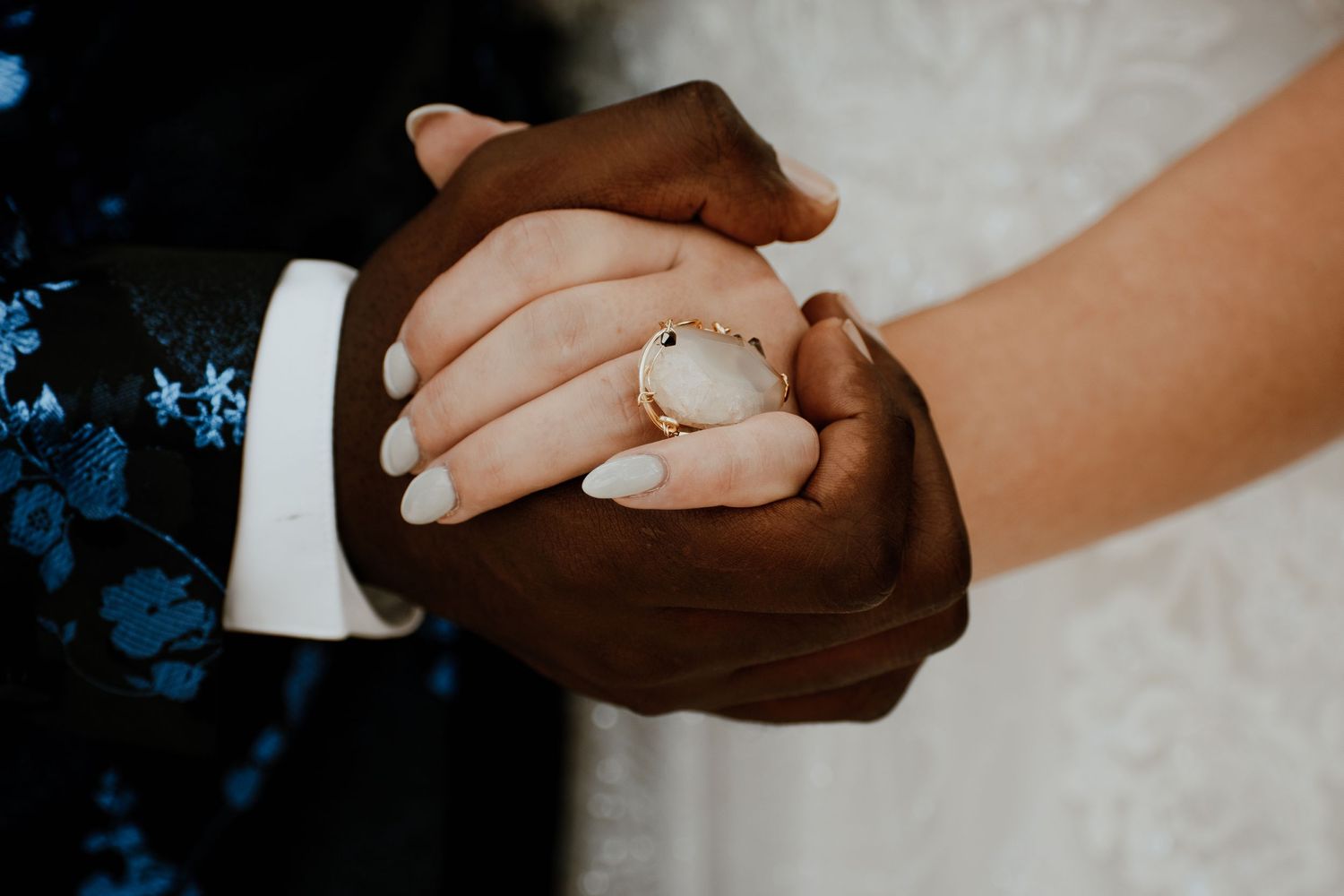 Close up of hands exchanging wedding rings against a light background.