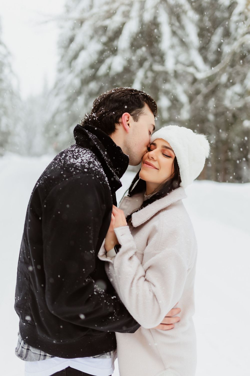 Romantic winter scene with couple embracing in snowy forest.