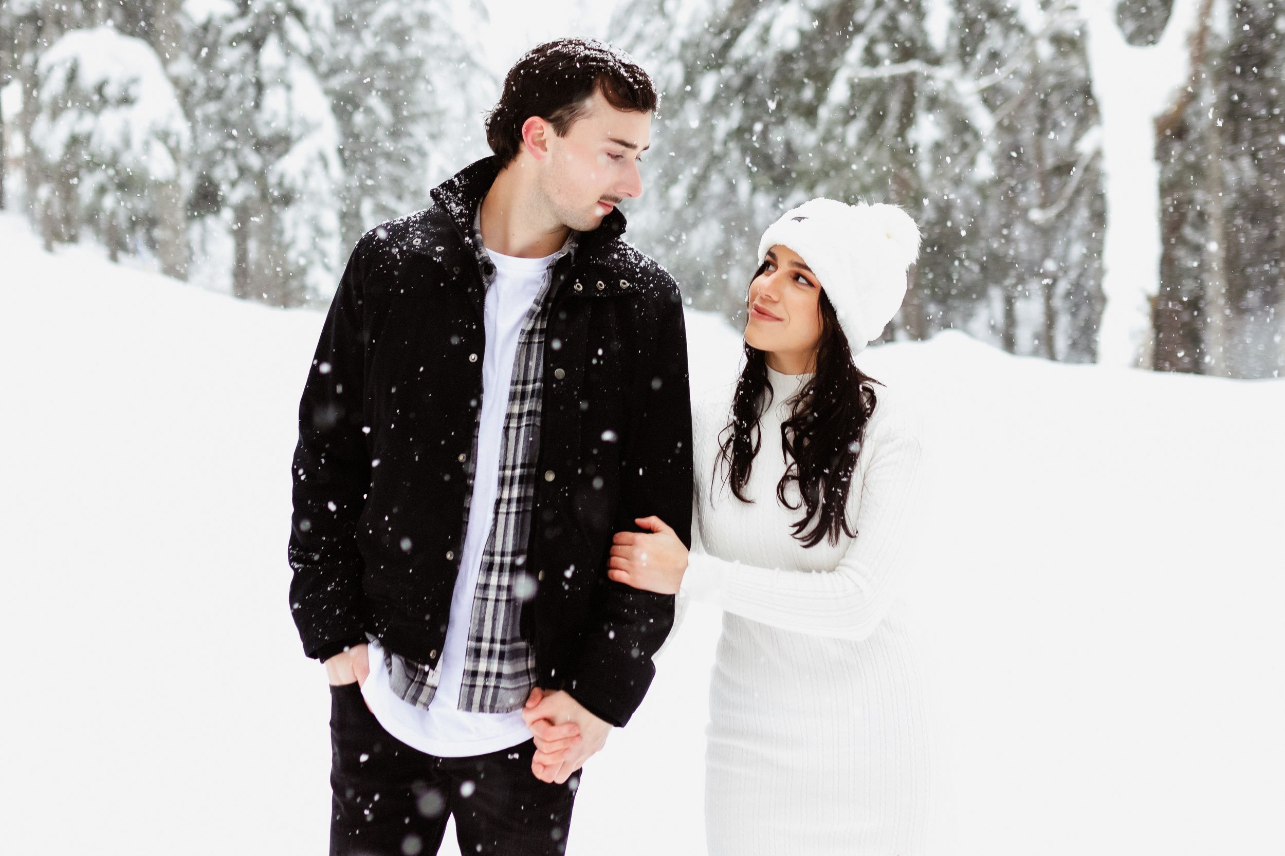 Winter photoshoot with couple in contrasting black and white outfits against snowy forest.