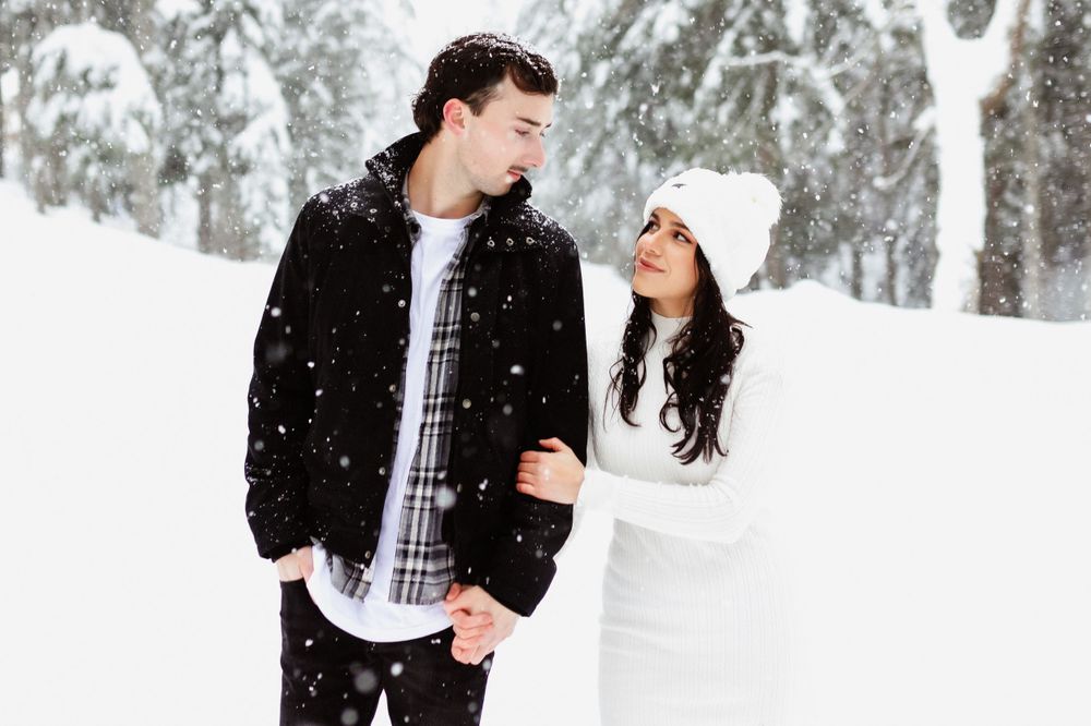 Winter photoshoot with couple in contrasting black and white outfits against snowy forest.
