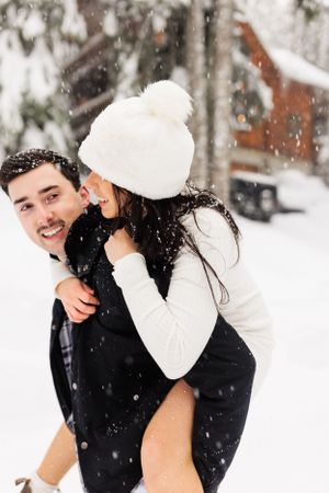 Playful piggyback ride moment in snowy winter setting.