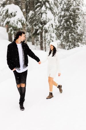 Playful couple walking through snow-covered forest path.