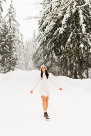Person in white dress twirling joyfully in snowy forest.