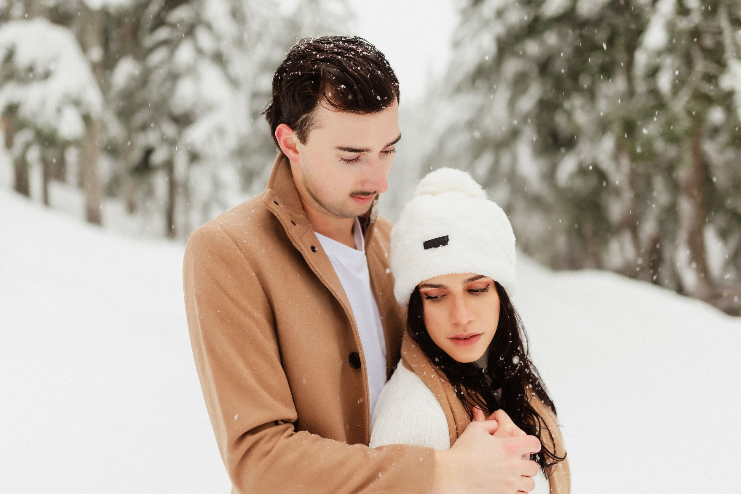Winter portrait of couple in casual outerwear against snow-covered trees.
