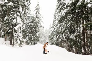 Romantic winter scene with couple embracing among snow-laden evergreen trees.