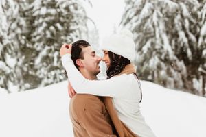 A romantic winter embrace between a couple in the snow surrounded by snow-covered evergreen trees.