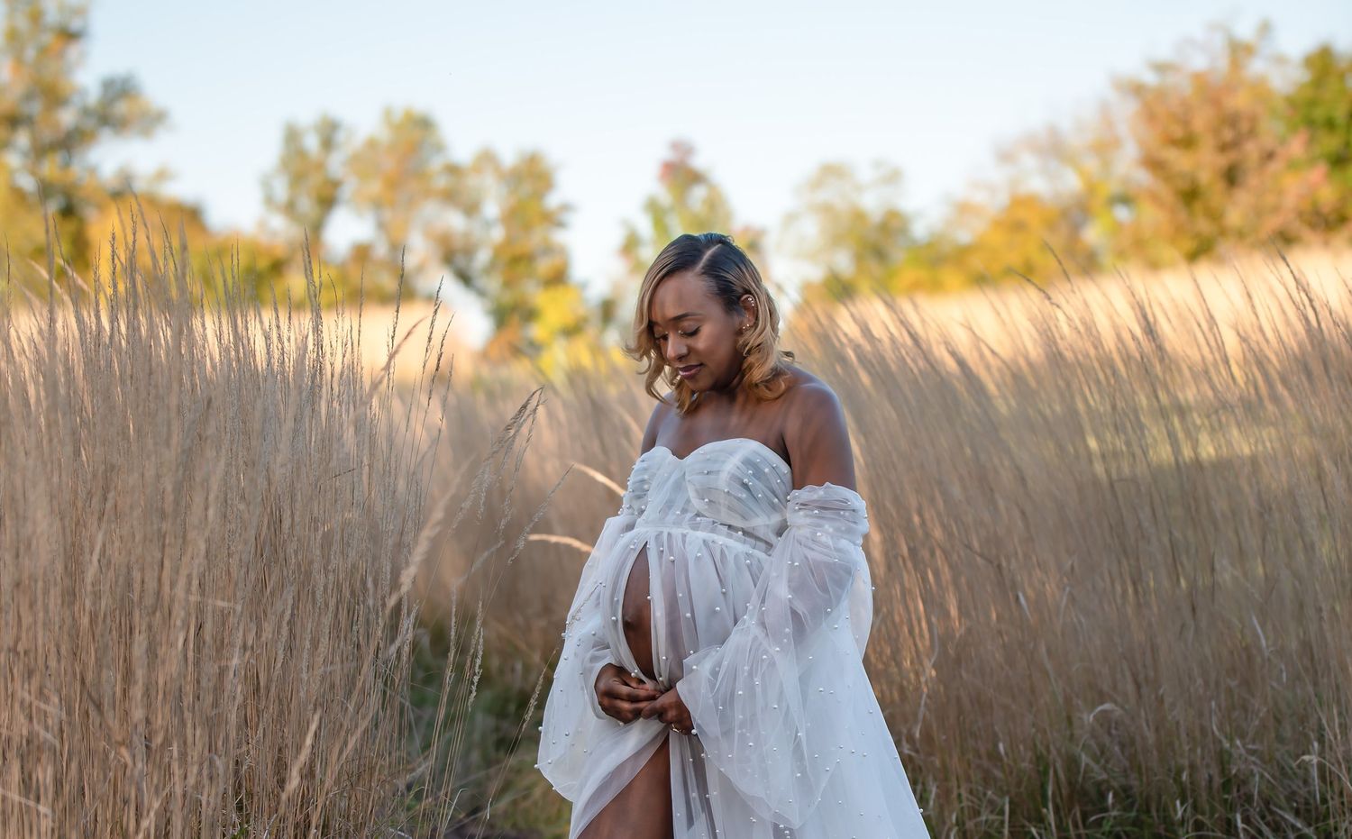 Dreamy maternity photos in a sunlit field of tall grass at sunset.