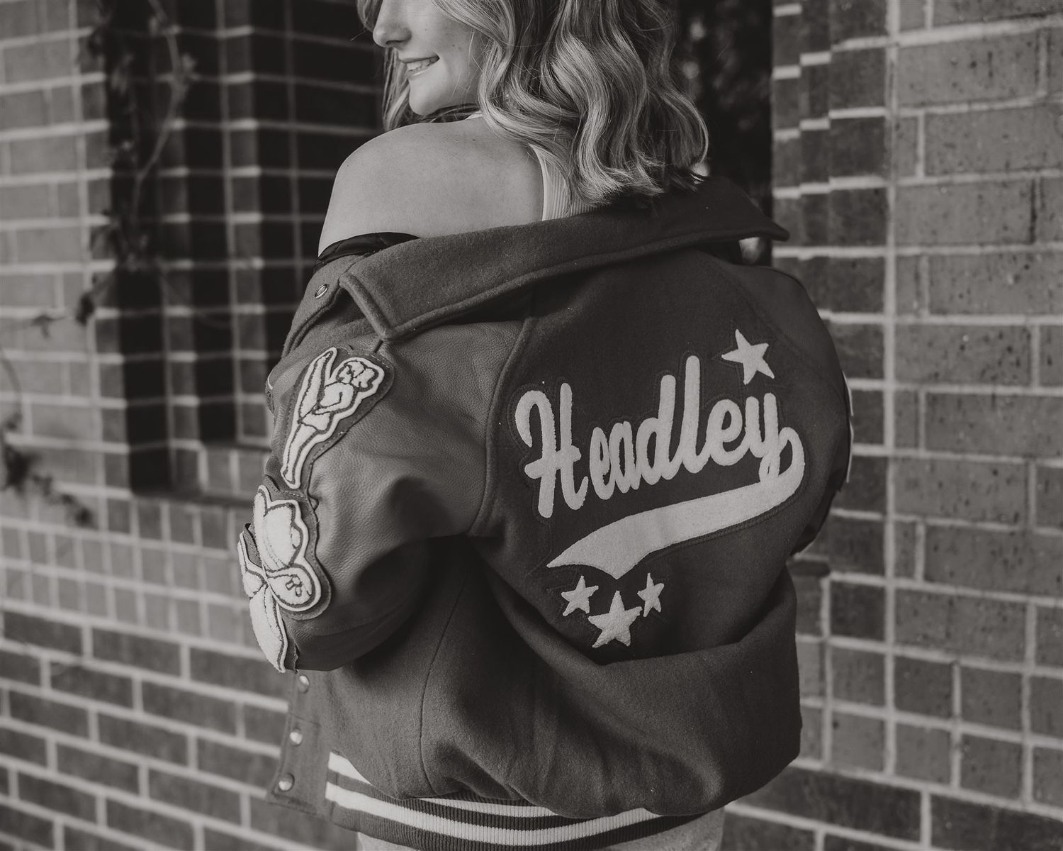 Black and white detail shot of a varsity jacket with 'Headley' lettering and decorative patches.