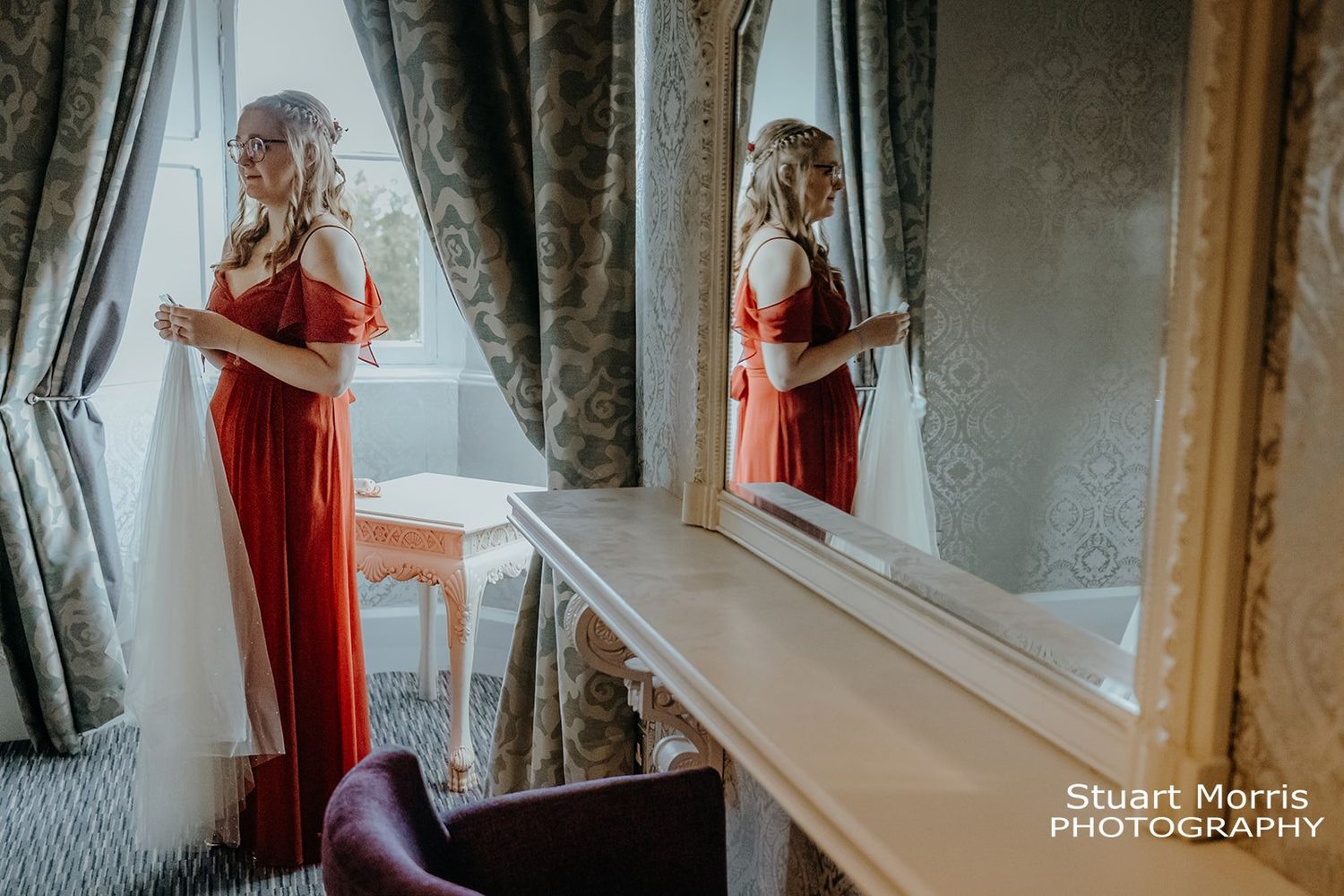 bridesmaid holding the brides veil reflected in a mirror during the wedding prep. Ruthin castle wedding photographer.
