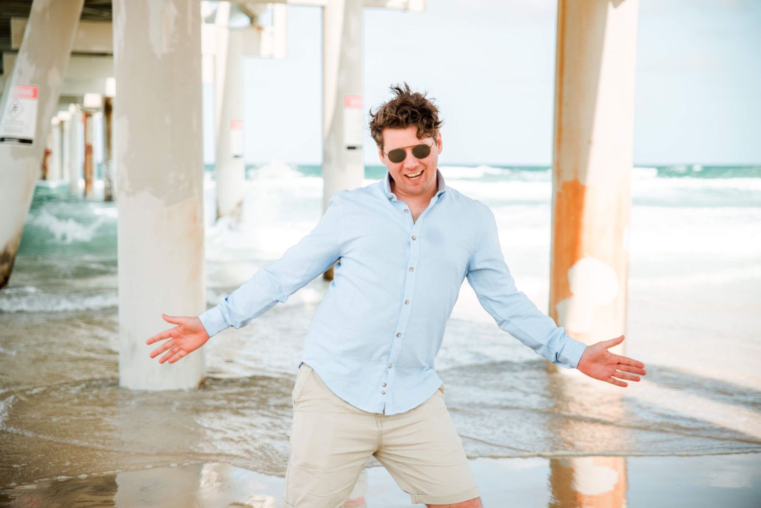 A playful moment on the beach with someone in a light blue button-down shirt and khaki shorts gesturing.