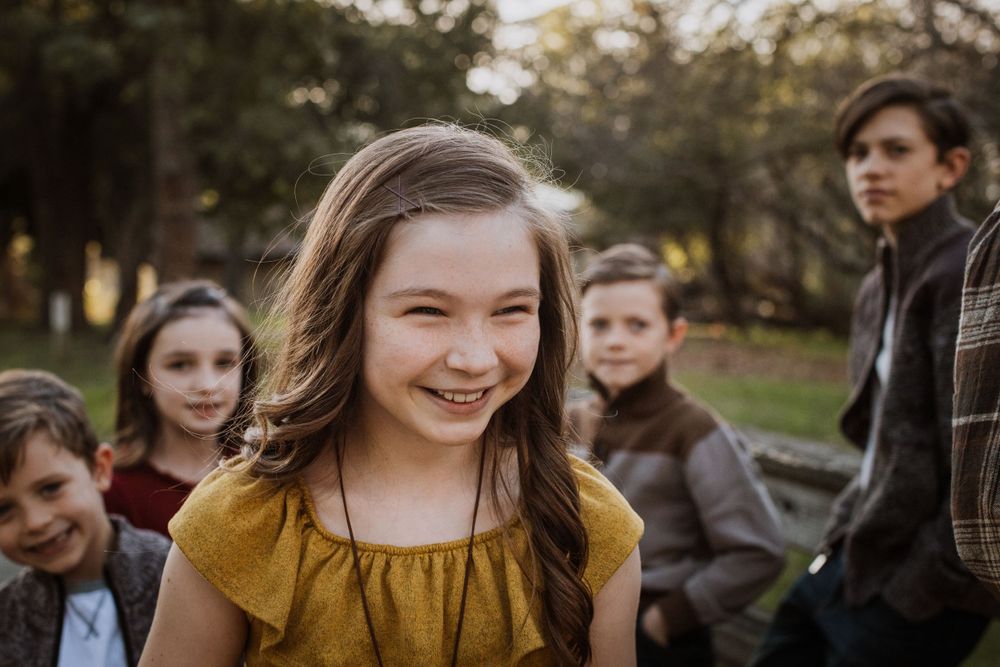 Person in yellow dress smiling brightly outdoors with others in background.