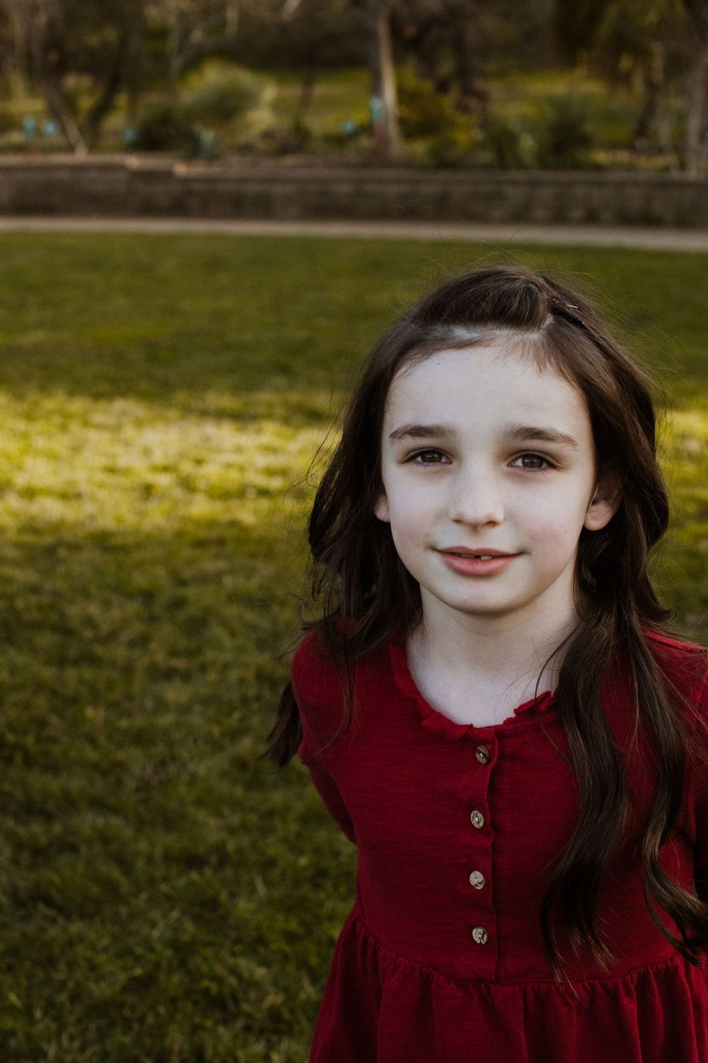 A portrait in a garden setting featuring a burgundy dress with buttons and long dark hair.