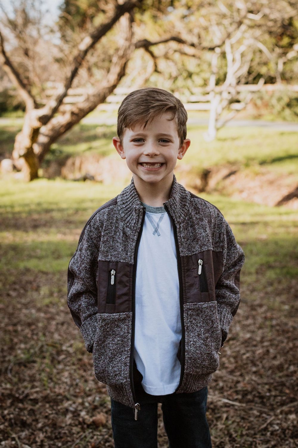 A casual portrait showing a grey zip-up jacket against a natural outdoor backdrop.