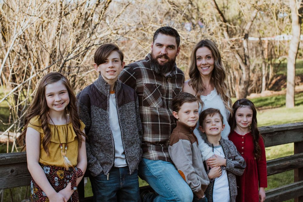 Family group portrait on wooden fence with rustic outdoor background.